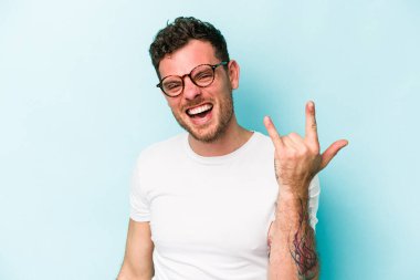 Mavi arka planda izole edilmiş genç beyaz adam boynuzlarını devrim konsepti olarak gösteriyor..