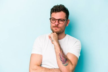 Kafkasyalı genç adam mavi arka planda izole edilmiş şüpheli, belirsiz, seni muayene ediyor..