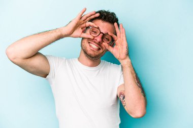 Mavi arka planda izole edilmiş genç beyaz adam gözlerinde sorun olmadığını gösteriyor.