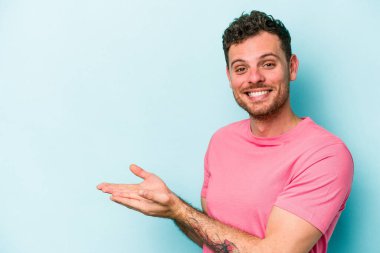 Mavi arka planda izole edilmiş genç beyaz bir adam palmiyesinde bir kopya alanı tutuyor..