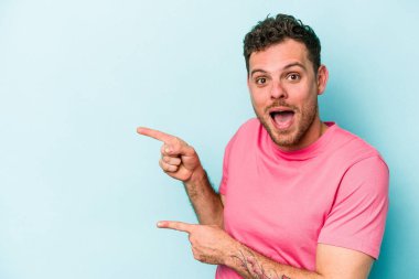 Kafkasyalı genç adam mavi arka planda izole edilmiş. İşaret parmağıyla işaret ettiği için heyecanlı..