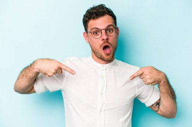 Kafkasyalı genç adam mavi arka planda izole edildi. Parmakları aşağıda, olumlu bir his var..