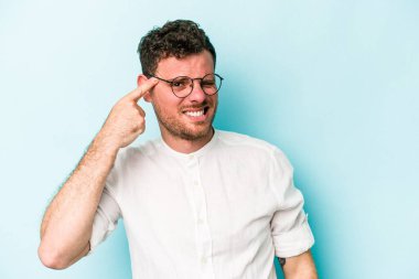 Mavi arka planda izole edilmiş genç beyaz adam kulaklarını elleriyle kapatıyor..