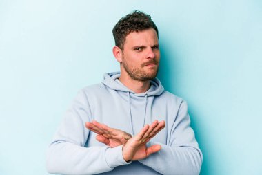 Kafkasyalı genç adam mavi arka planda izole edilmiş bir şekilde inkar hareketi yapıyor.