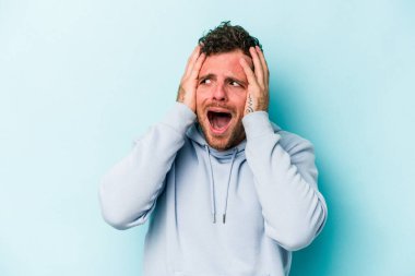 Kafkasyalı genç adam mavi arka planda izole edilmiş kulakları kulaklarıyla kapatıyor çok fazla ses duymamaya çalışıyor..