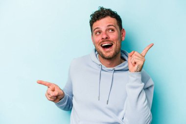 Mavi arka planda izole edilmiş genç beyaz adam farklı kopya alanlarını gösteriyor, birini seçiyor, parmaklarıyla gösteriyor.