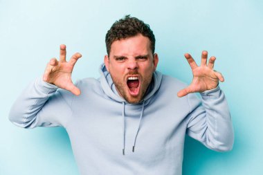 Mavi arka planda izole edilmiş genç beyaz adam pençelerini kedi taklidi yaparken gösteriyor, agresif bir hareket..