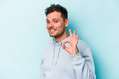 Kafkasyalı genç bir adam mavi arka planda izole edilmiş bir şekilde göz açıp kapayana kadar iyi bir el hareketi yapıyor..