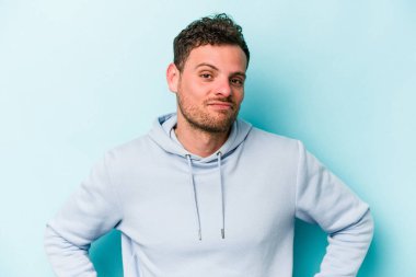 Kafkasyalı genç adam mavi arka planda izole edilmiş üzgün, ciddi yüzlü, mutsuz ve hoşnutsuz..