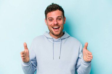 Mavi arka planda izole genç beyaz adam iki eliyle bir şey tutuyor, ürün sunumu..