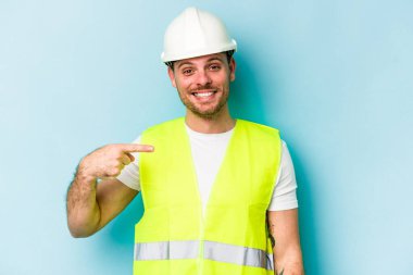 Beyaz tenli genç işçi, mavi arka planda izole edilmiş. Elle bir gömlek fotokopi alanını gösteriyor. Gururlu ve kendinden emin.
