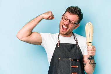 Kafkasyalı genç kunduracı mavi arka planda izole edilmiş zafer kazandıktan sonra yumruğunu kaldırıyor, kazanan konsept.