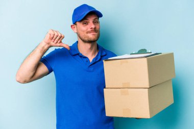 Mavi arka planda izole edilmiş genç beyaz teslimatçı gururlu ve kendinden emin hissediyor, örnek olarak.
