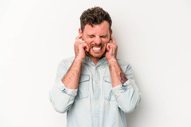 Beyaz arka planda izole edilmiş genç beyaz bir adam kulaklarını elleriyle kapatıyor..