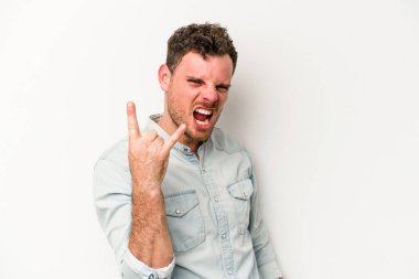 Beyaz arka planda izole edilmiş genç beyaz bir adam parmaklarıyla kaya hareketi gösteriyor.