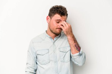 Beyaz arka planda izole olmuş genç beyaz bir adam başı ağrıyor, yüzüne dokunuyor..