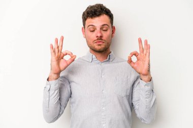 Beyaz arka planda izole edilmiş genç beyaz adam yoğun bir günün ardından rahatlıyor. Yoga yapıyor..