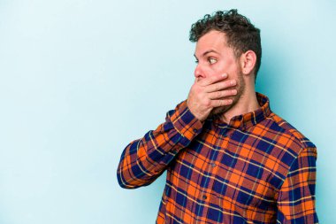 Kafkasyalı genç adam mavi arka planda izole edilmiş. Düşünceli bir şekilde ağzıyla ağzını kapatan bir fotokopi odasına bakıyor..