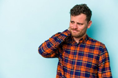 Kafkasyalı genç adam mavi arka planda izole edilmiş kafasının arkasına dokunuyor, düşünüyor ve bir seçim yapıyor..