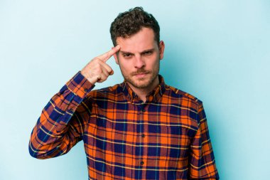 Mavi arka planda izole edilmiş genç beyaz bir adam şakağı parmağıyla işaret ediyor, düşünüyor ve bir göreve odaklanıyor..
