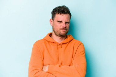 Mavi arka planda izole edilmiş genç beyaz adam alaycı bir ifadeyle kameraya bakarken mutsuz oluyor..