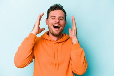 Kafkasyalı genç adam mavi arka planda izole edilmiş neşeli bir şekilde gülüyor. Mutluluk kavramı.