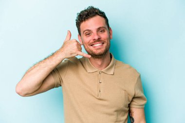 Mavi arka planda izole edilmiş genç beyaz adam parmaklarıyla bir cep telefonu hareketi gösteriyor..