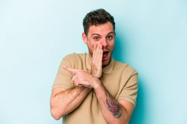 Kafkasyalı genç adam mavi arka planda izole edilmiş. Dedikodu yapıyor, bir şeyleri bildiriyor..