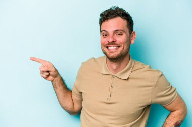 Mavi arka planda izole edilmiş genç beyaz adam işaret parmağıyla işaret ederek gülümsüyor..