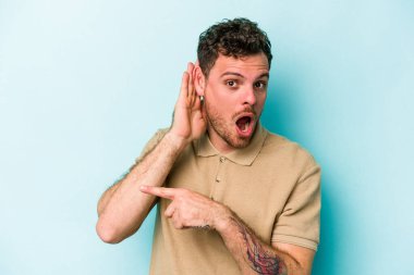 Mavi arka planda izole edilmiş genç beyaz adam bir dedikoduyu dinlemeye çalışıyor..