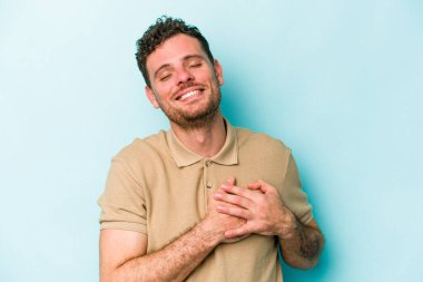 Mavi arka planda izole edilmiş beyaz bir genç, dost bir ifadeye sahip, avuçlarını göğsüne bastırıyor. Aşk konsepti.