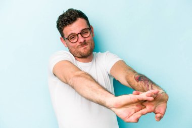 Mavi arka planda izole edilmiş genç beyaz adam kollarını uzatıyor, rahat bir konumda..
