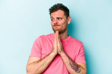 Kafkasyalı genç adam mavi arka planda izole edilmiş dua ediyor, bağlılık gösteriyor, dindar biri ilahi ilham arıyor..
