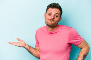 Mavi arka planda izole edilmiş genç beyaz bir adam bir palmiye üzerinde fotokopi alanı ve belinde bir el daha gösteriyor..