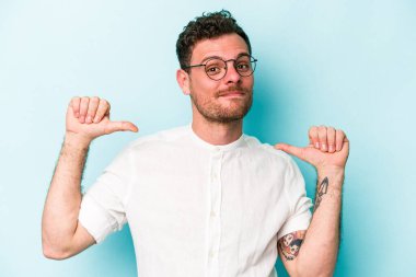 Mavi arka planda izole edilmiş genç beyaz adam gururlu ve kendinden emin hissediyor, örnek olarak.