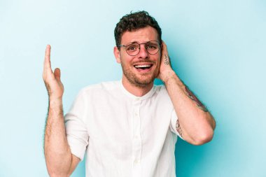 Mavi arka planda izole edilmiş genç beyaz adam öfkeyle bağırıyor..