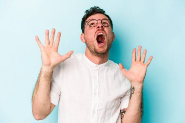 Kafkasyalı genç adam mavi arka planda izole edilmiş gökyüzüne haykırıyor, yukarı bakıyor, hayal kırıklığına uğramış..