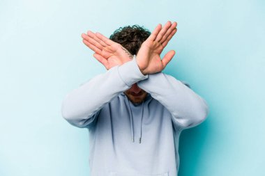 Kafkasyalı genç adam mavi arka planda izole edilmiş iki kolu çapraz tutuyor, inkar kavramı.