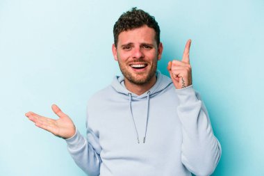 Kafkasyalı genç adam mavi arka planda izole edilmiş ve elinde bir ürün tutuyor..