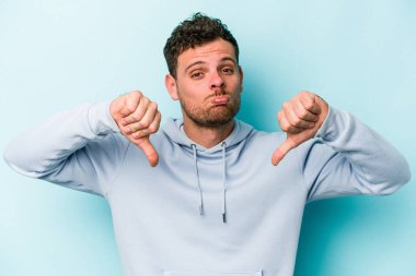 Mavi arka planda izole edilmiş genç beyaz bir adam hoşlanmadığı bir jest yapıyor. Anlaşmazlık konsepti.
