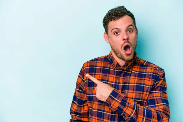 Mavi arka planda izole edilmiş genç beyaz adam yan tarafı işaret ediyor.