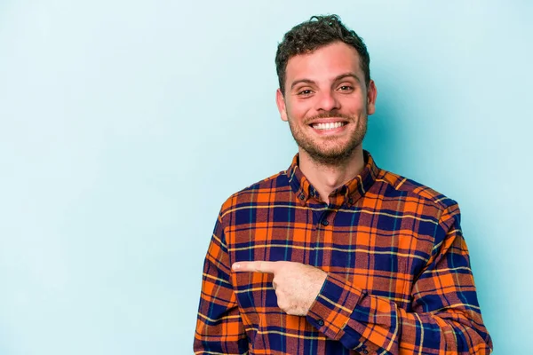 Mavi arka planda izole edilmiş genç beyaz adam gülümsüyor ve boş alanda bir şeyler gösteriyor..