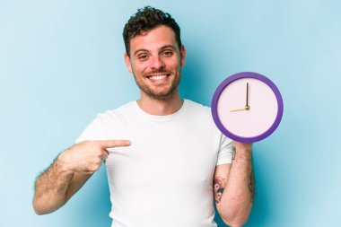 Elinde mavi arka planda bir saat tutan genç, beyaz bir adam gömleğin fotokopi alanını elle işaret ediyor, gururlu ve kendinden emin.