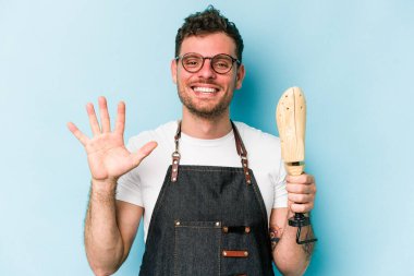 Kafkasyalı genç kunduracı mavi arka planda izole edilmiş beş numarayı parmaklarıyla gülümsüyor..