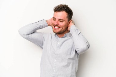 Beyaz arka planda izole olmuş genç beyaz bir adam kendini güvende hissediyor, elleri başının arkasında..