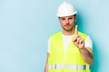Genç işçi beyaz adam mavi arka planda izole edildi. Bir numarayı parmağıyla gösteriyor..