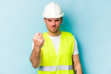 Young laborer caucasian man isolated on blue background showing fist to camera, aggressive facial expression.