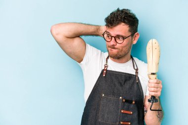 Kafkasyalı genç kunduracı mavi arka planda izole edilmiş kafasının arkasına dokunuyor, düşünüyor ve bir seçim yapıyor..