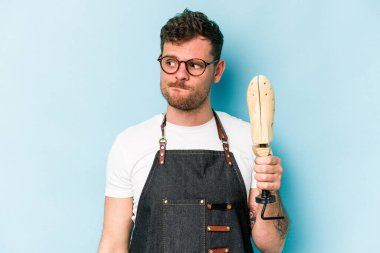 Kafkasyalı genç kunduracı mavi arka planda izole edilmiş, kafası karışmış, şüpheli ve güvensiz hissediyor..