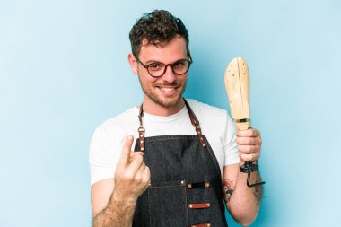 Kafkasyalı genç kunduracı, mavi arka planda izole edilmiş ve sanki seni davet ediyormuş gibi parmağıyla işaret ediyor..